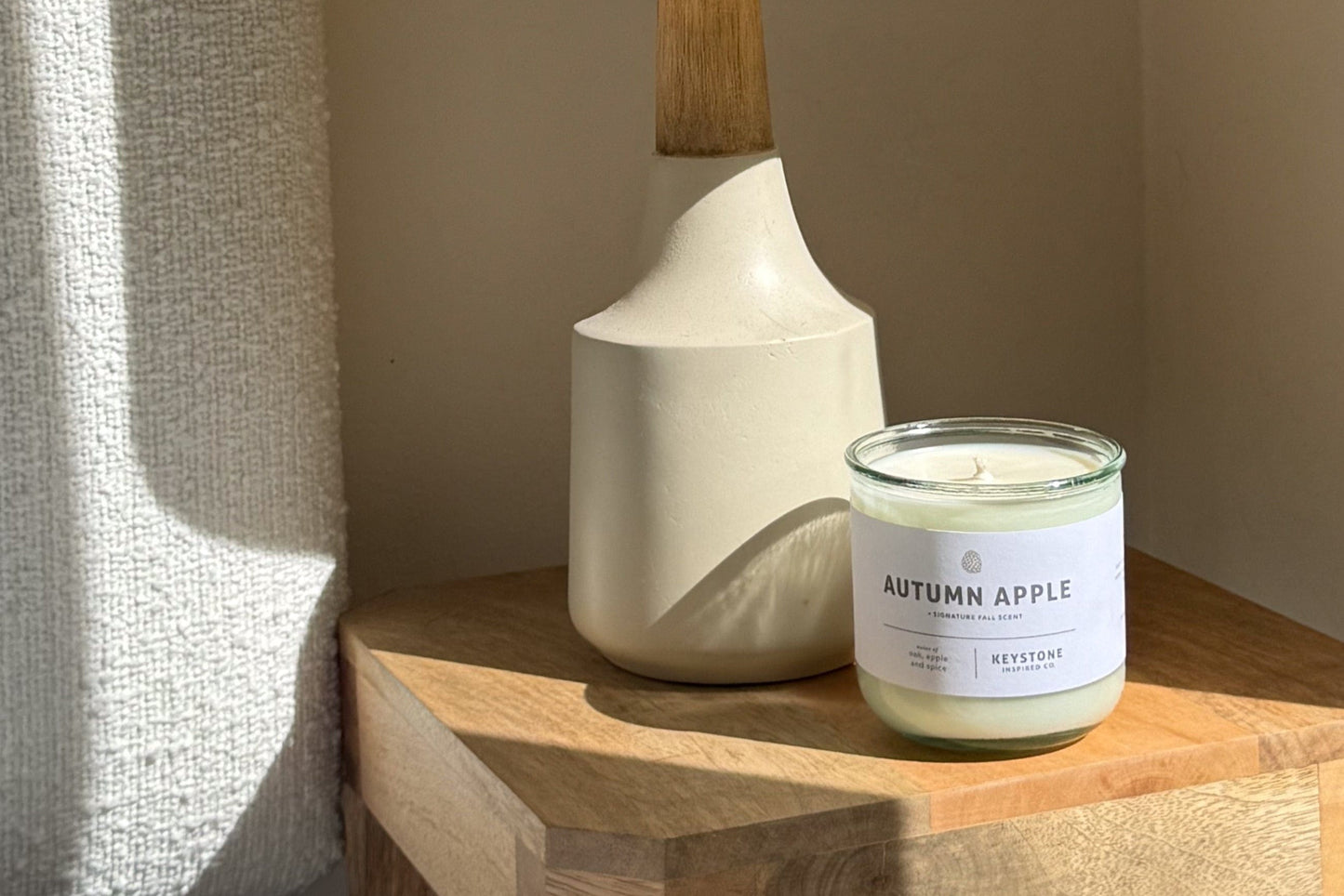 Candle labeled 'Autumn Apple' on a wooden surface next to a lamp.