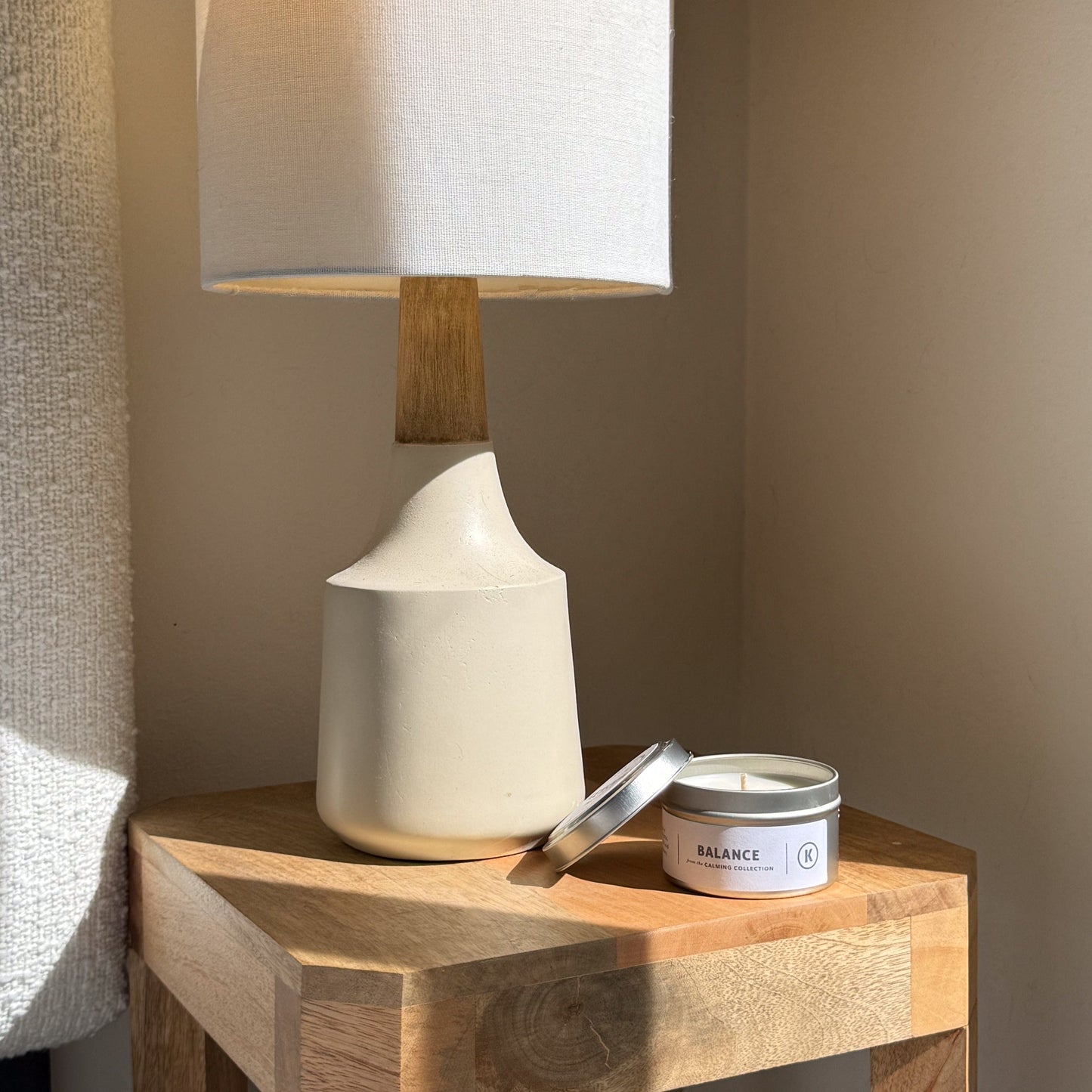 White ceramic lamp and candle on a wooden side table against a neutral wall.