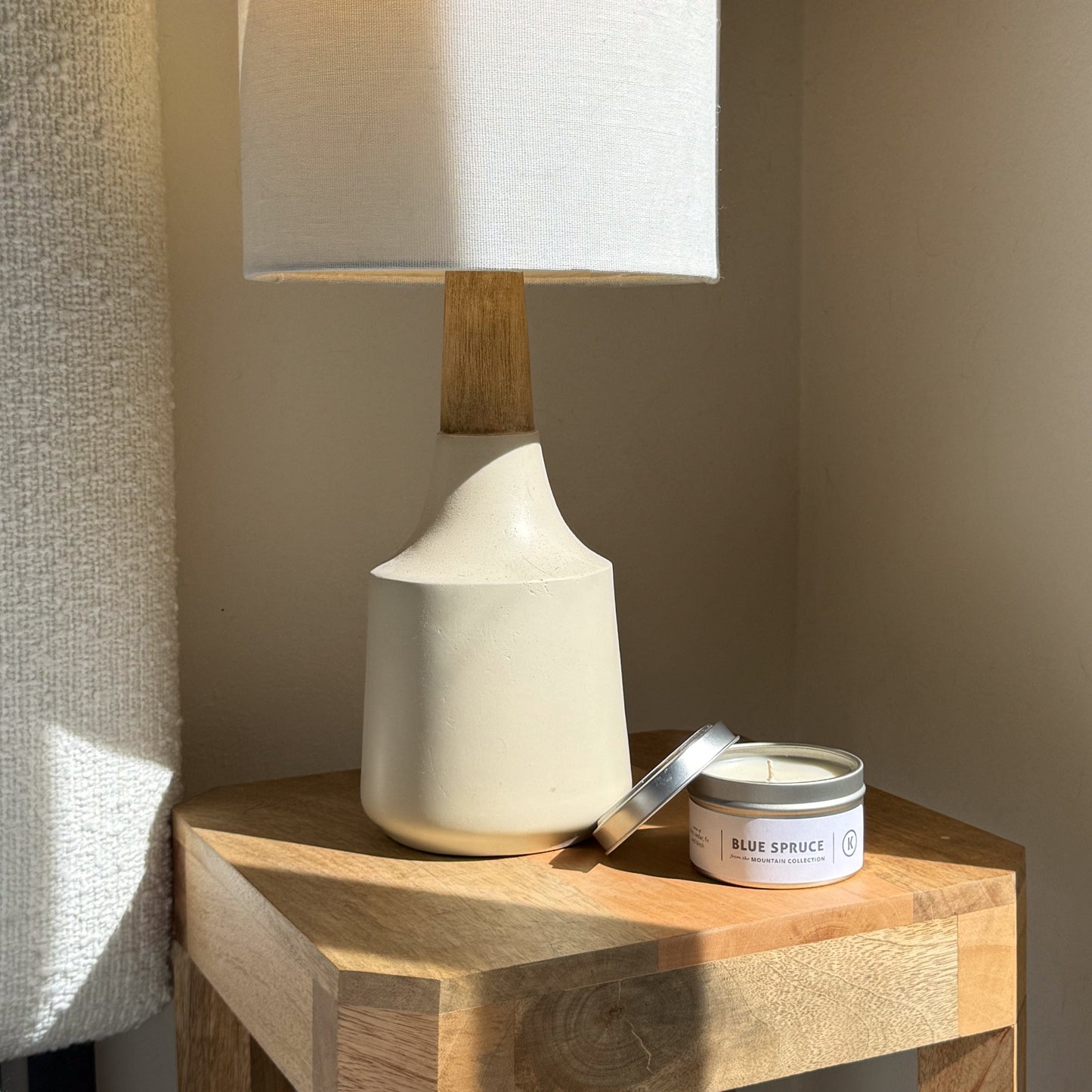 White ceramic lamp and candle on a wooden side table against a neutral wall.