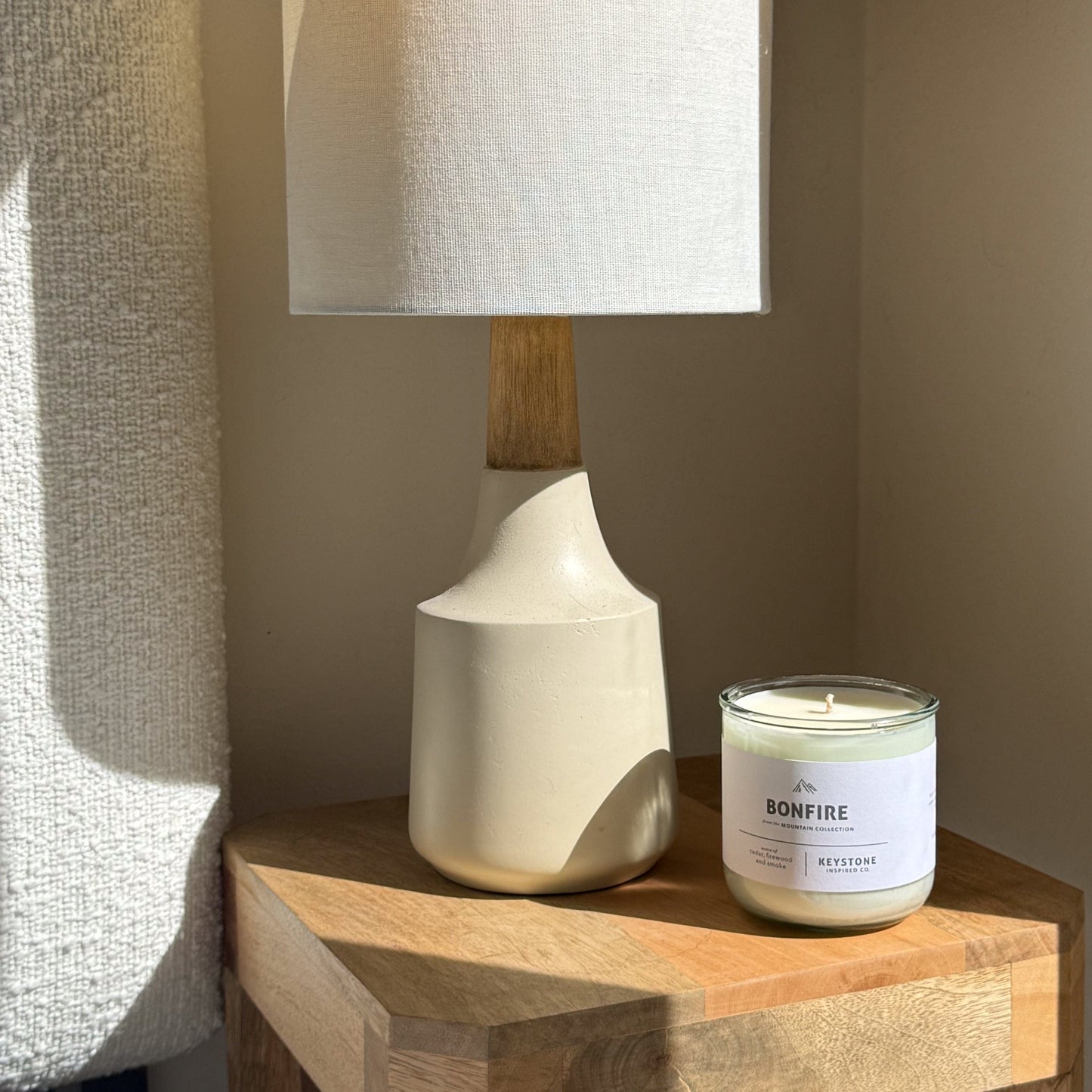 White ceramic lamp and 'Bonfire' candle on a wooden surface with a neutral background