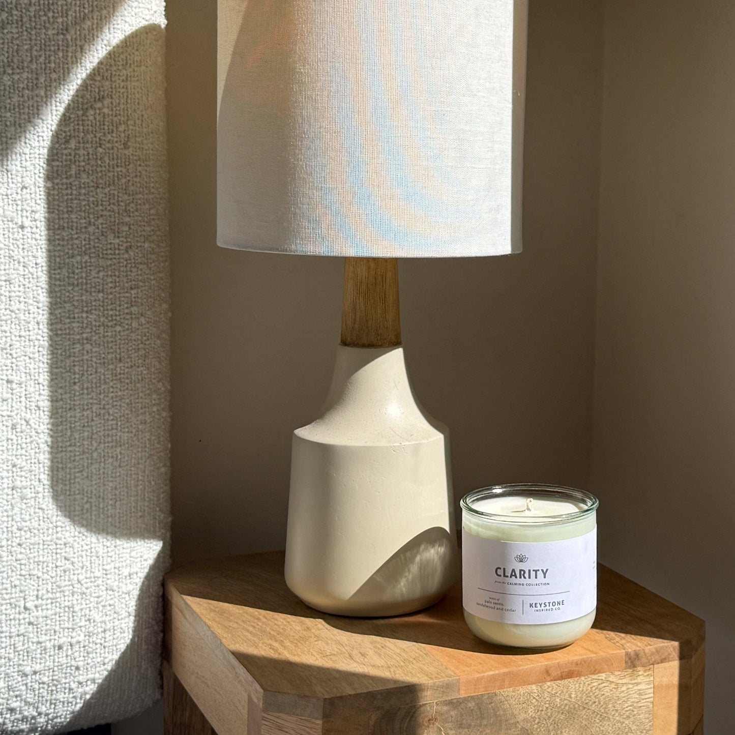 Candle labeled 'Clarity' next to a lamp on a wooden surface with a neutral background