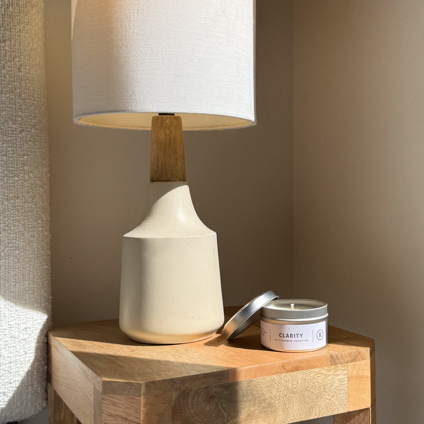 White table lamp with wooden base on a wooden surface next to a candle labeled 'Clarity'.