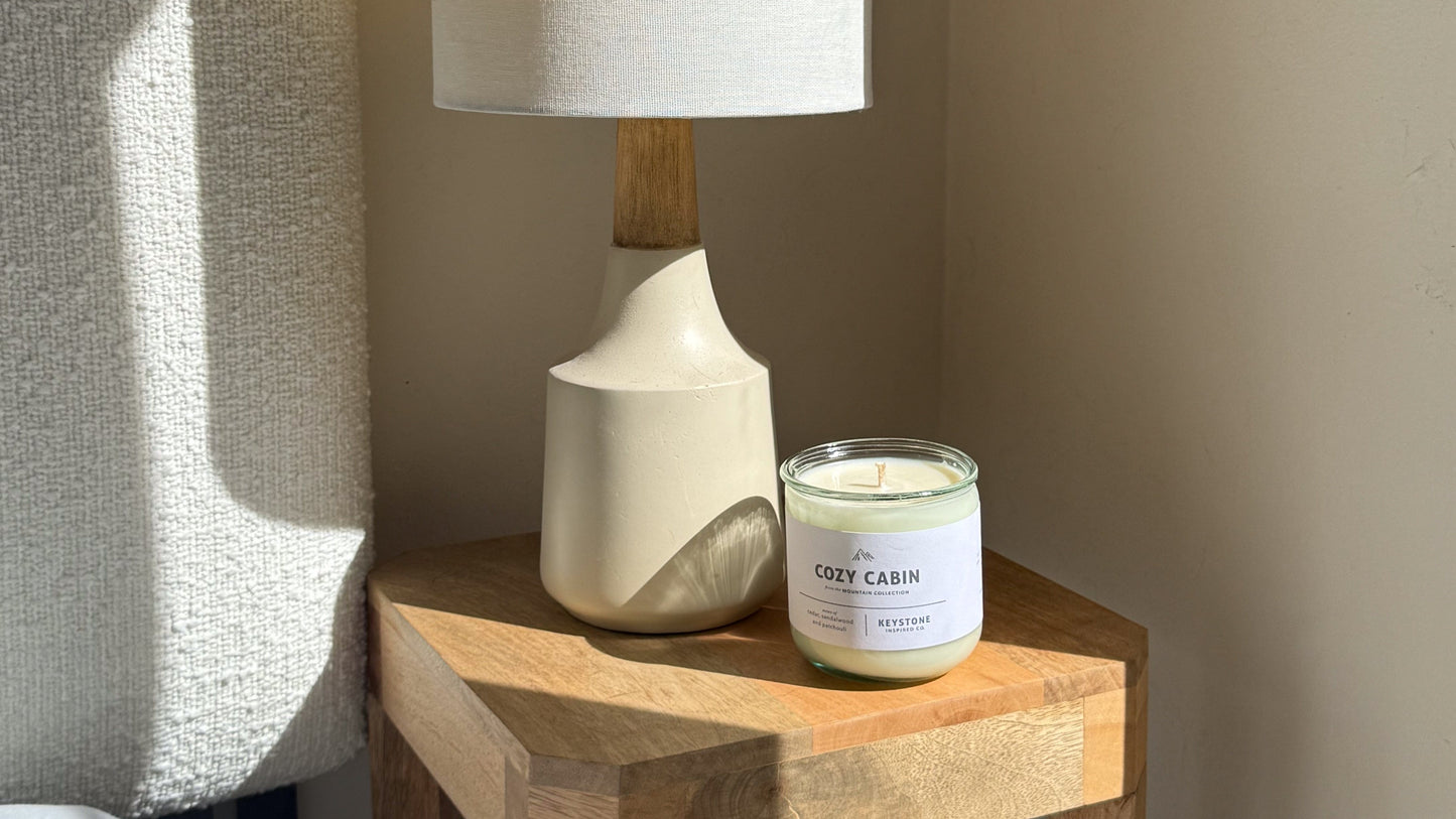 Table lamp with a white shade and wooden base on a nightstand next to a candle.