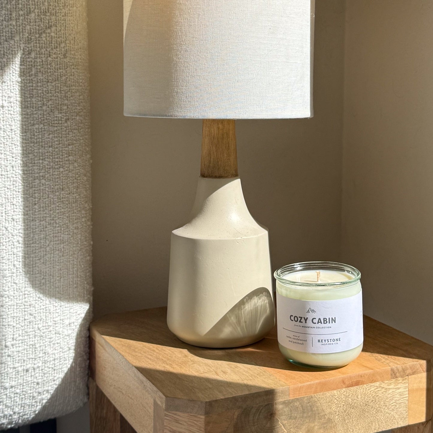 Candle labeled 'Cozy Cabin' next to a lamp on a wooden surface.
