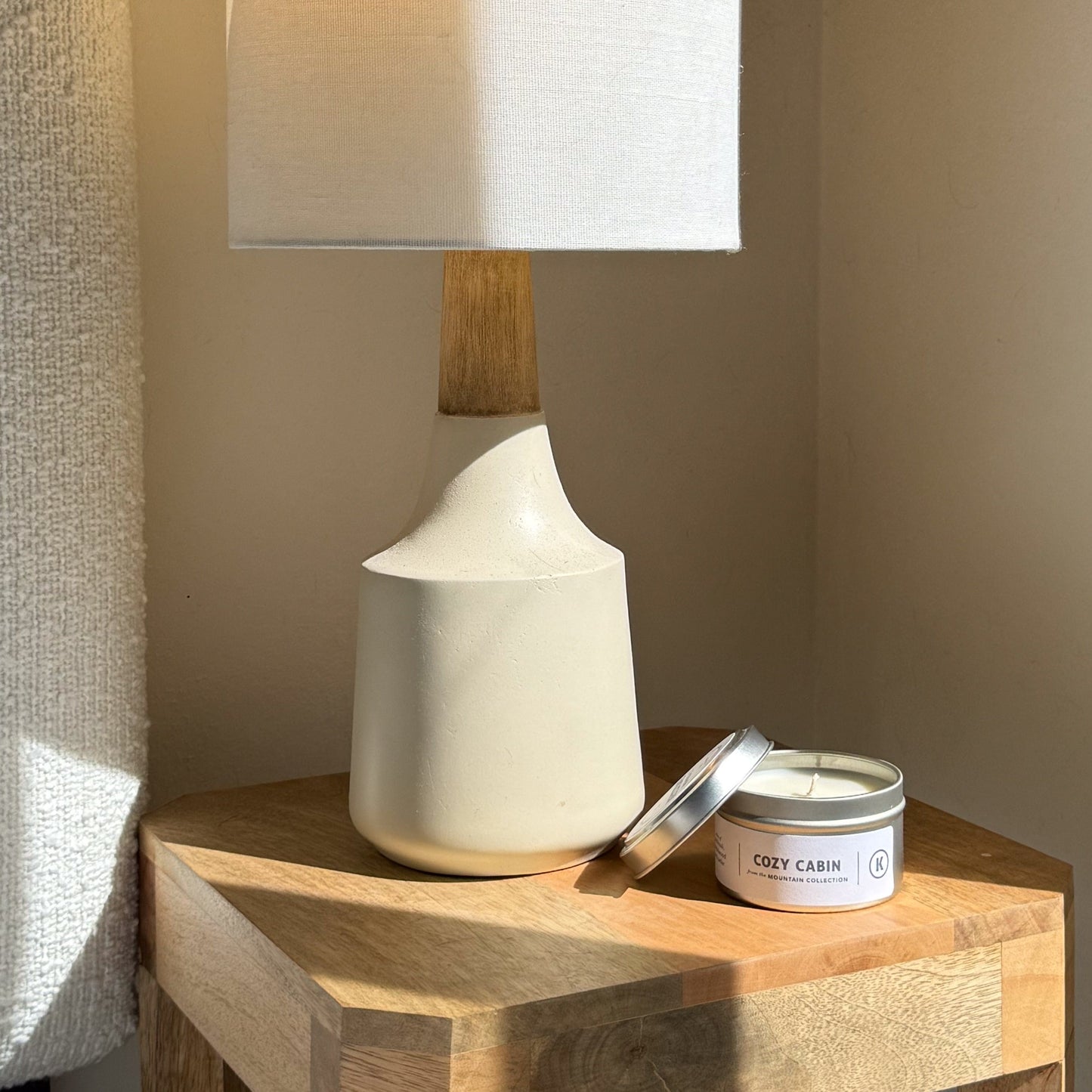 White ceramic lamp on a wooden side table with a 'Cozy Cabin' candle.