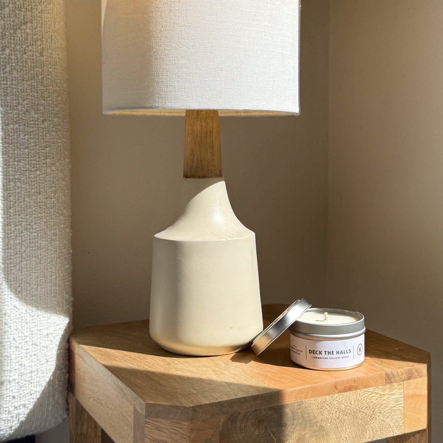 White lamp with wooden base on a wooden surface next to a candle