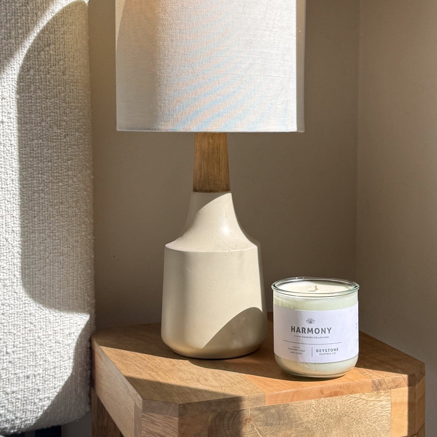 White ceramic lamp and 'Harmony' candle on a wooden surface with a neutral background