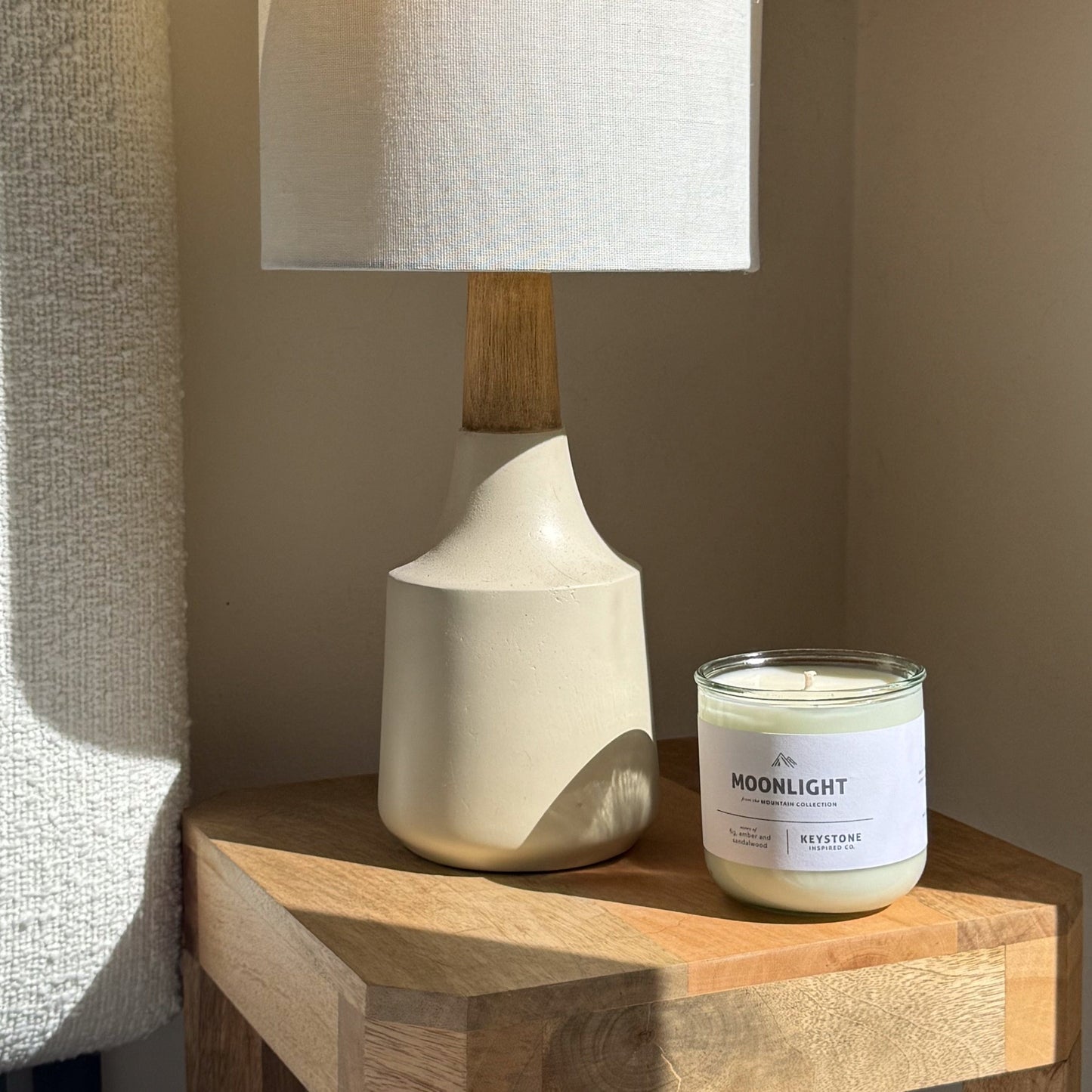Candle labeled 'Moonlight' next to a lamp on a wooden surface.