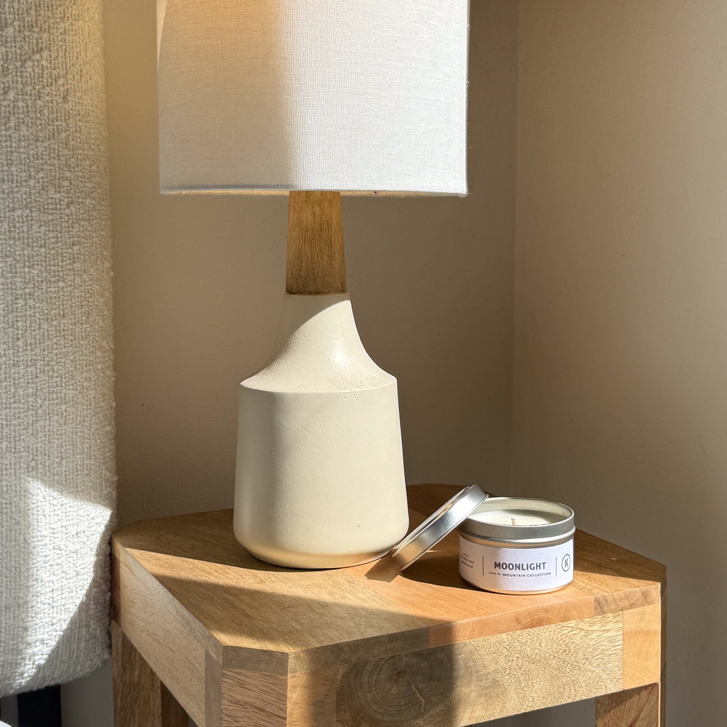 White ceramic lamp and candle on a wooden side table with soft lighting.