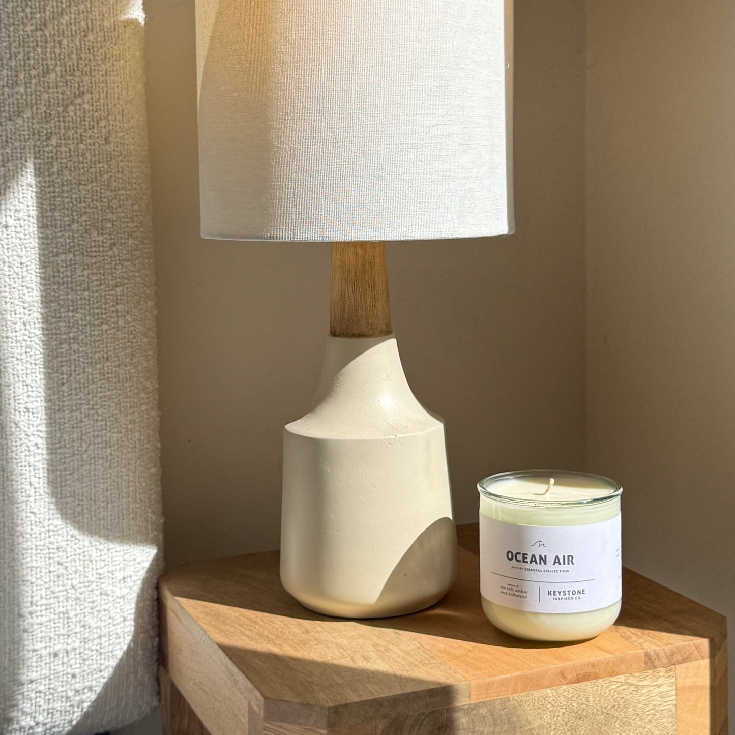 White ceramic lamp with wooden base next to a 'Ocean Air' candle on a wooden surface.