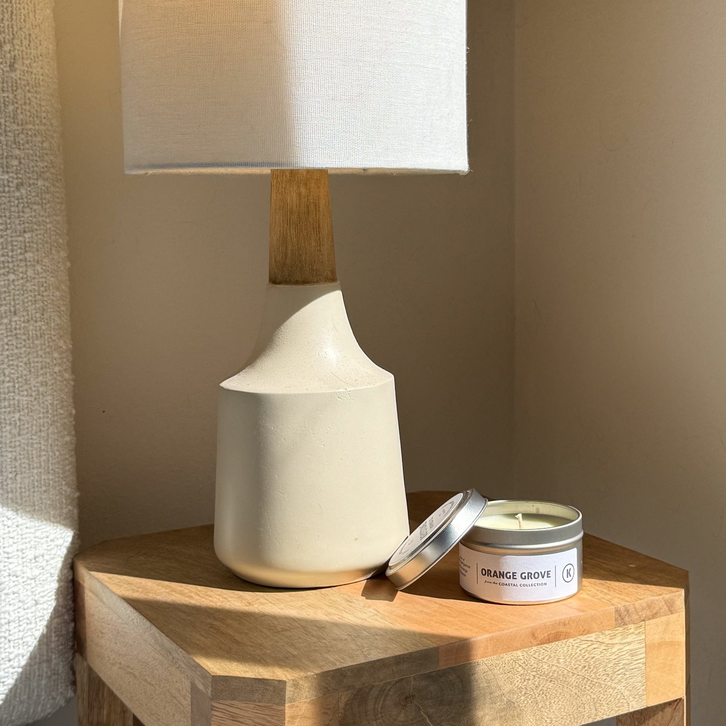 White ceramic lamp with wooden base on a wooden surface next to an 'Orange Grove' candle.