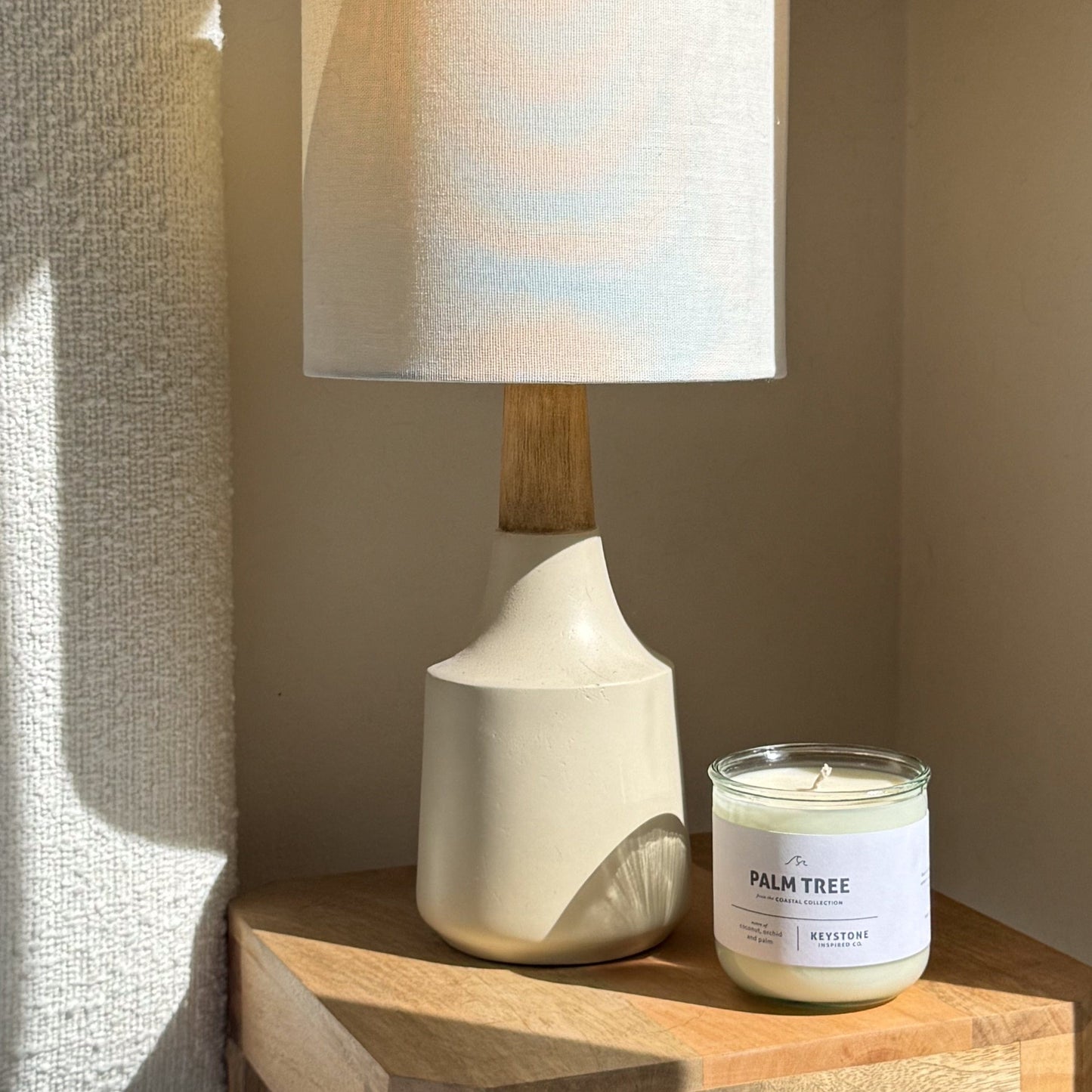 White ceramic lamp and 'Palm Tree' candle on a wooden surface with soft lighting.