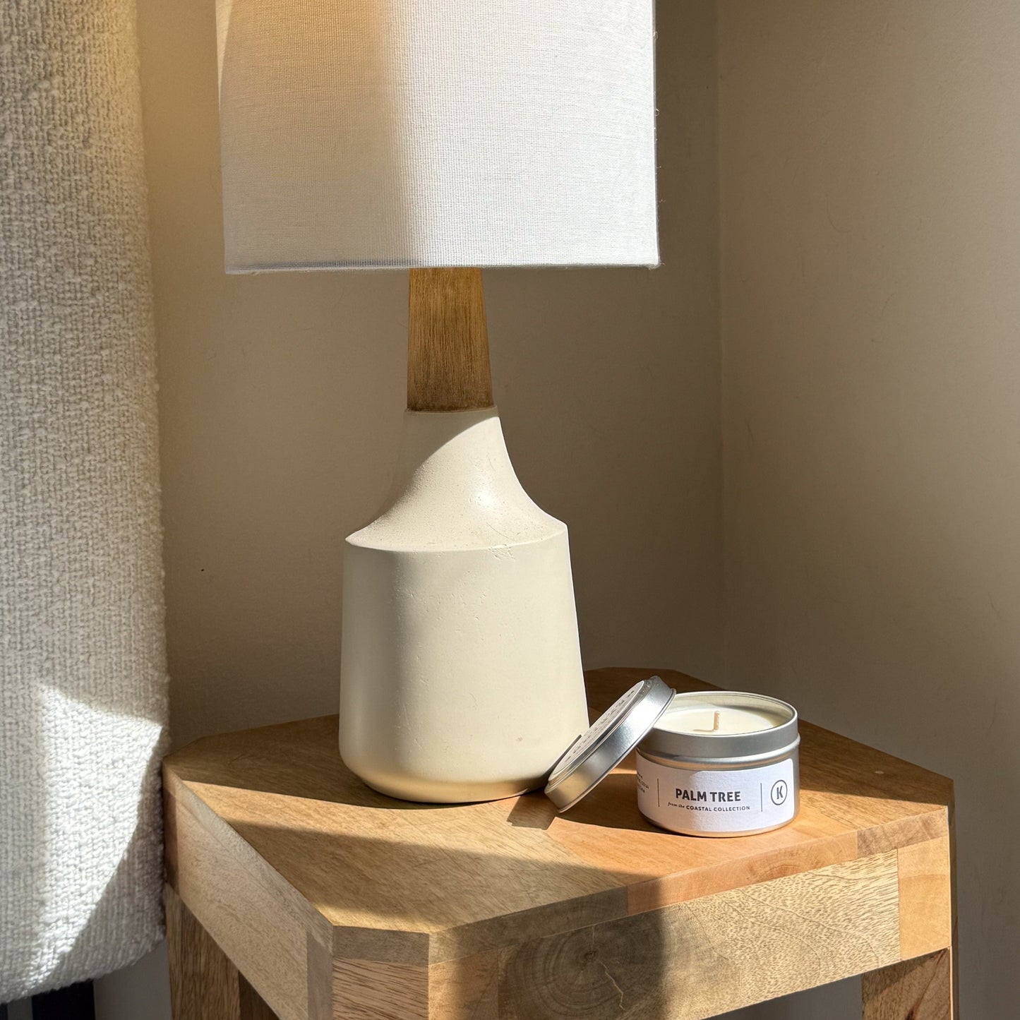 White ceramic lamp and palm tree candle on a wooden side table with a neutral background