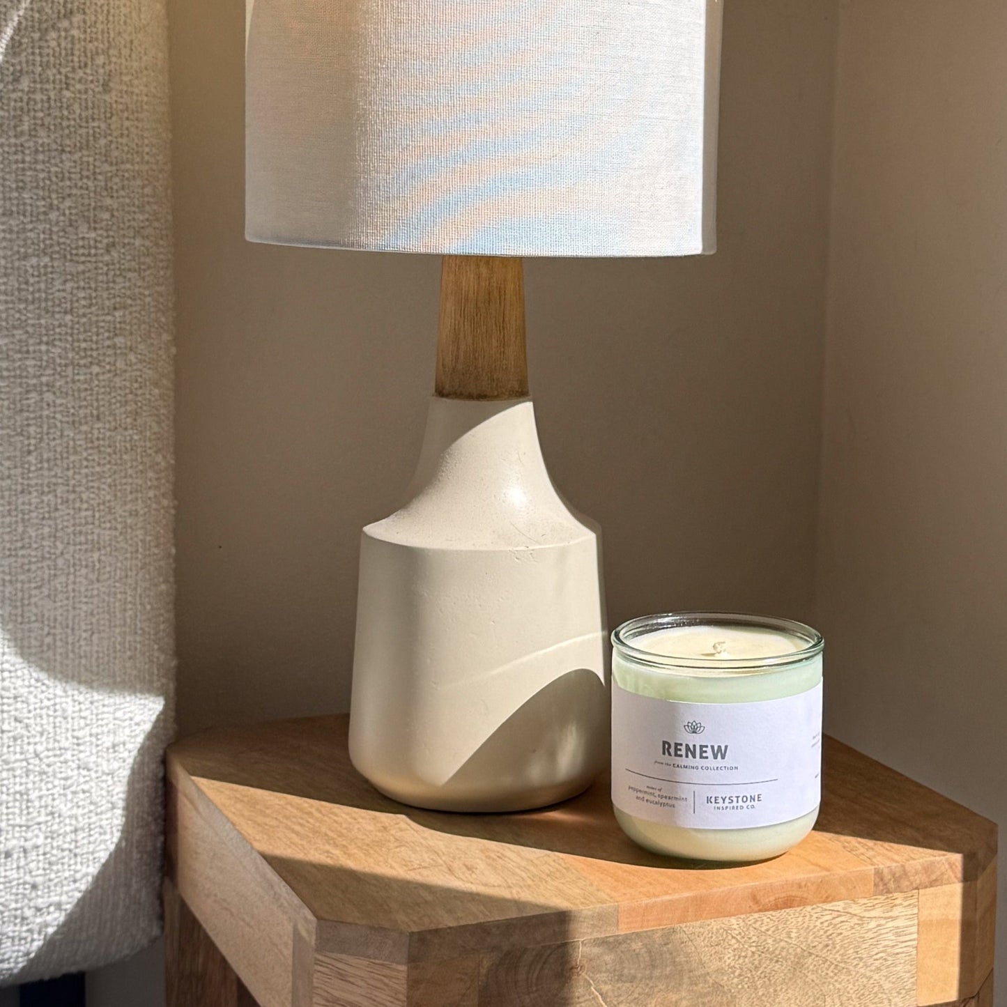 Candle labeled 'Renew' on a wooden surface next to a lamp.